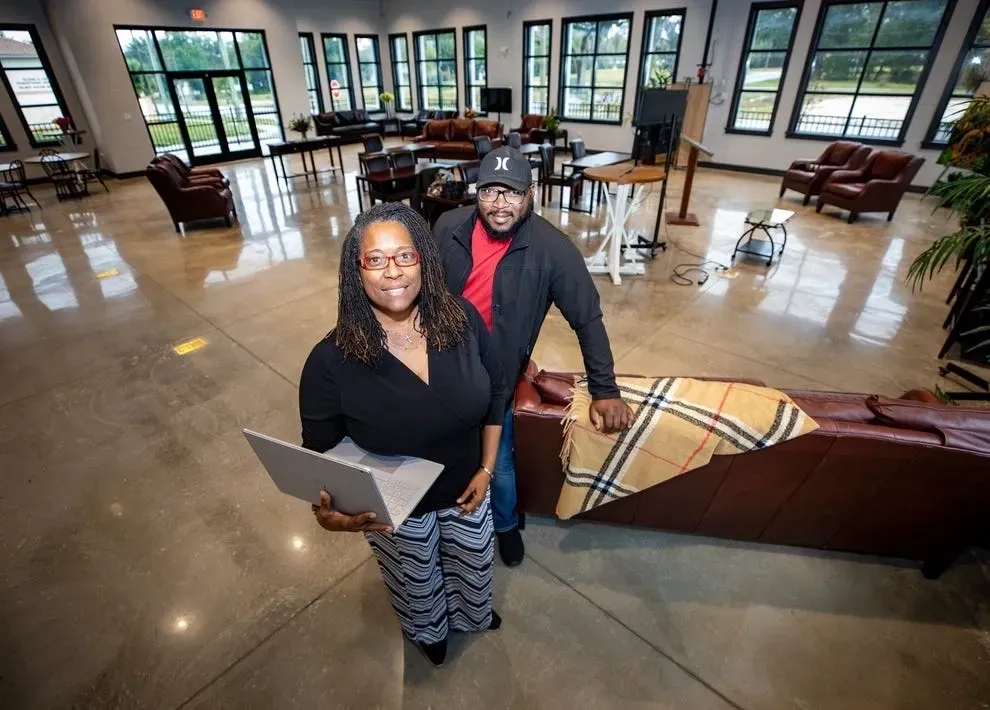 Two professionals standing in a modern office lobby, one holding a laptop.