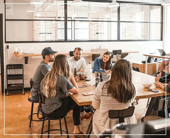 Group of people engaged in a casual meeting at a table in a modern office space.