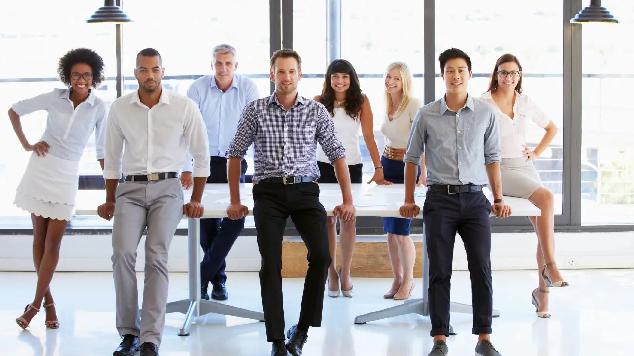 A diverse group of professionals standing and sitting in a bright, modern office space.