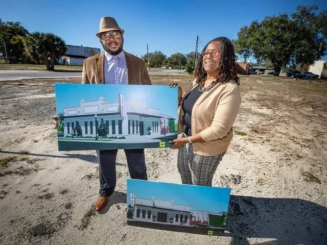 Two individuals standing outdoors holding architectural renderings of a building.